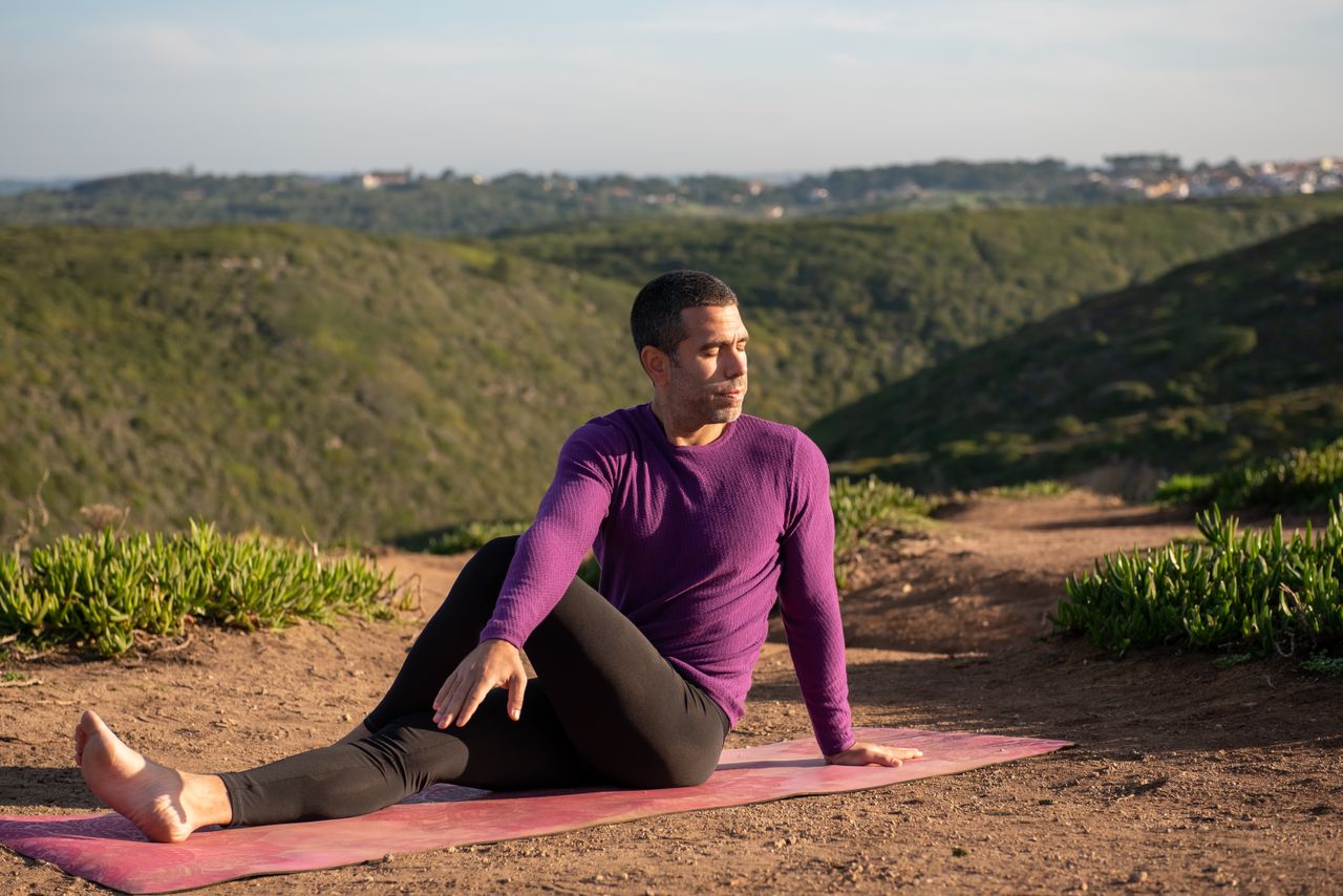 Menu Man practicing yoga outdoors in Portugal with lush green hills in the background.