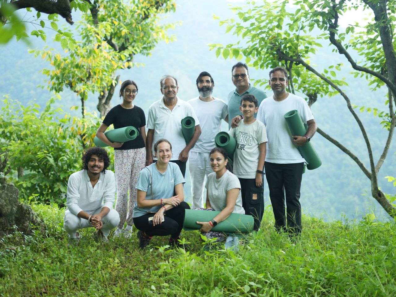 Home A diverse group enjoying an outdoor yoga retreat in the serene greenery of Rishikesh, India.