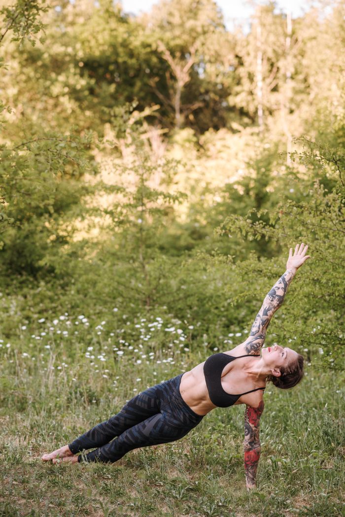 Menu Young slim female in sportswear standing in Vasisthasana pose while practicing yoga on grass and looking up