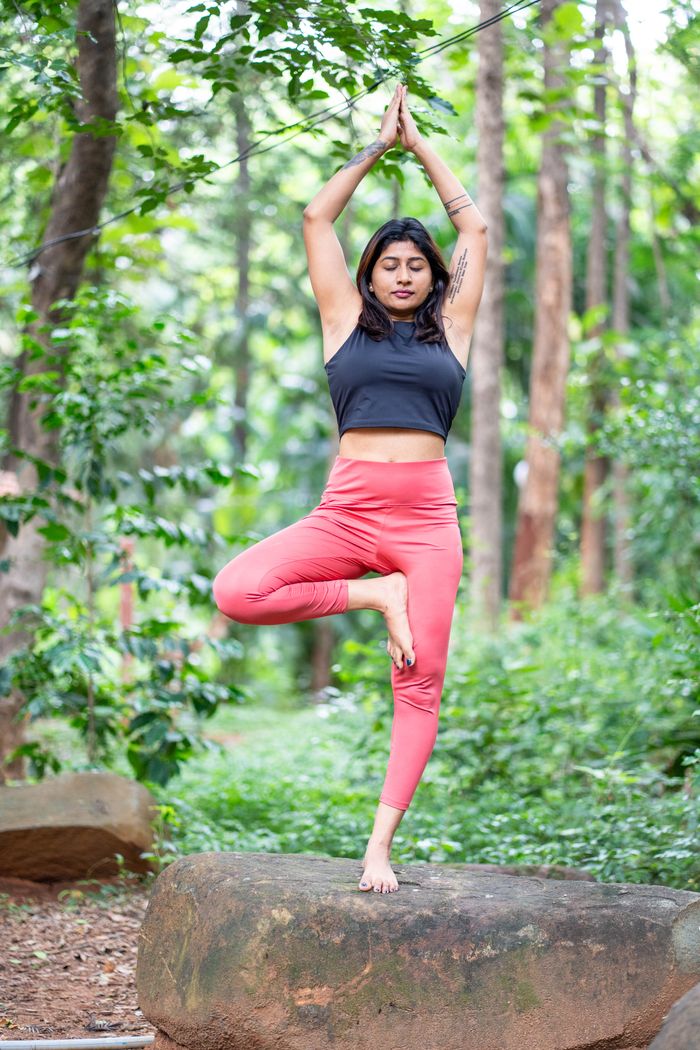 Home Female doing yoga tree pose on a rock in a lush forest setting, promoting mindfulness and fitness.