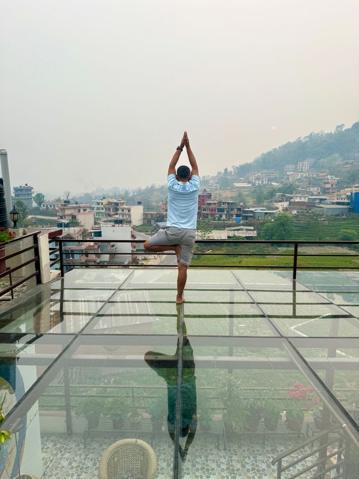 Home Man practicing yoga on a glass terrace with a scenic view of a hillside town.